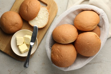 Photo of Fresh tasty buns in basket and butter on grey table, top view