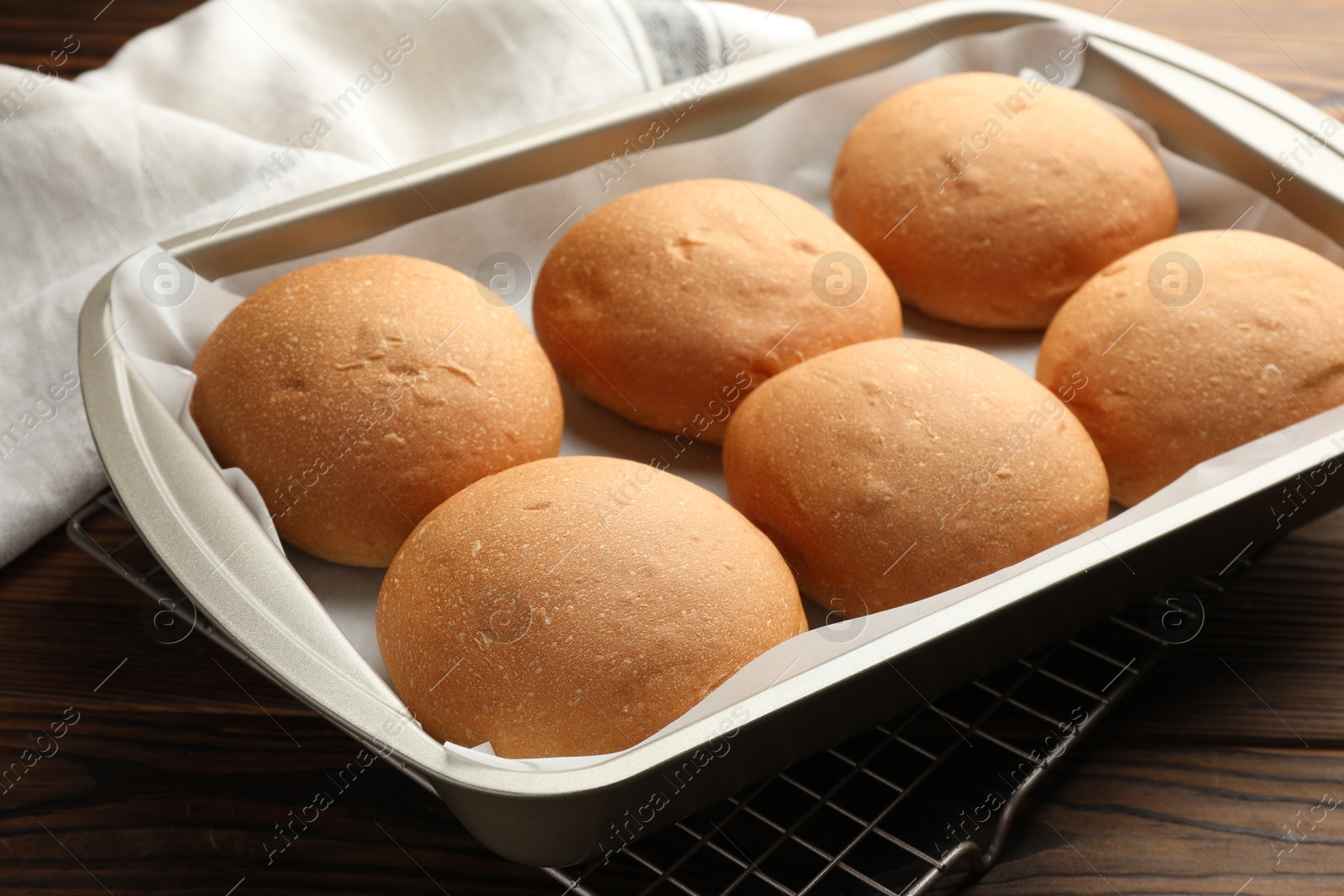 Photo of Fresh tasty buns in baking tray on wooden table, closeup