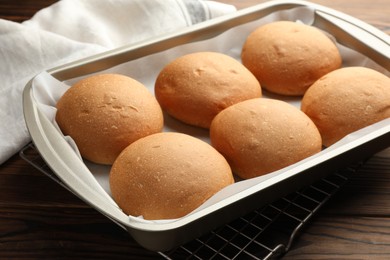 Photo of Fresh tasty buns in baking tray on wooden table, closeup