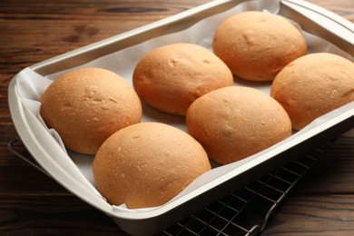 Photo of Fresh tasty buns in baking tray on wooden table, closeup