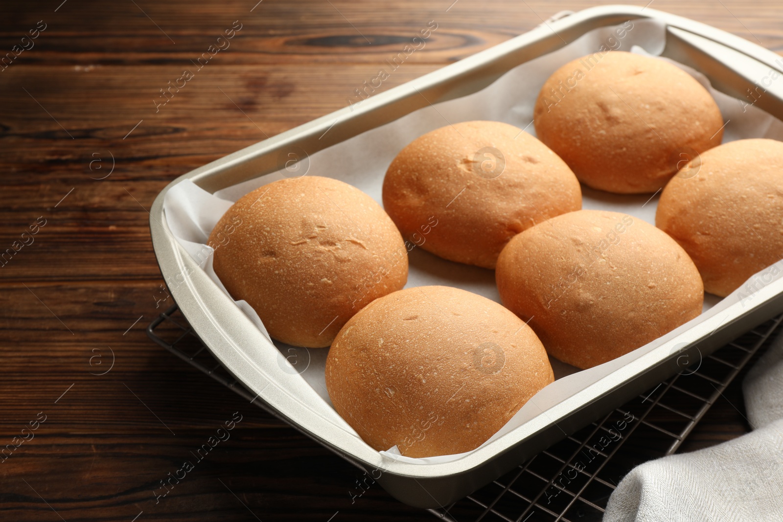 Photo of Fresh tasty buns in baking tray on wooden table, closeup