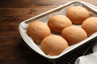 Photo of Fresh tasty buns in baking tray on wooden table, closeup