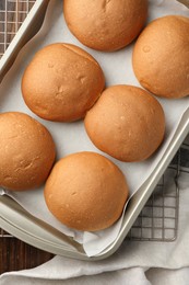 Photo of Fresh tasty buns in baking tray on table, top view