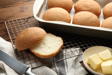 Photo of Fresh tasty buns, butter and knife on wooden table, closeup