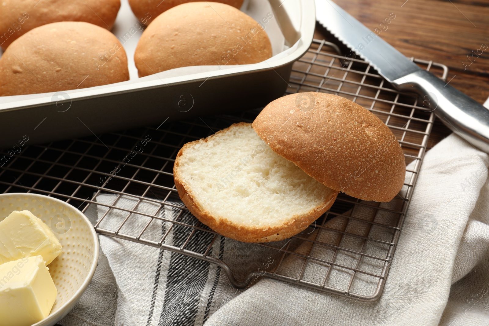 Photo of Fresh tasty buns, butter and knife on wooden table, closeup