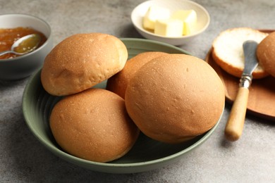 Photo of Fresh tasty buns, jam and butter on grey table, closeup