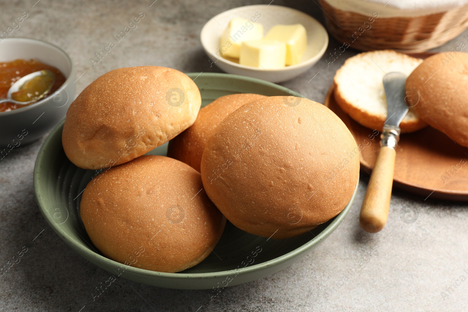 Photo of Fresh tasty buns, jam and butter on grey table, closeup