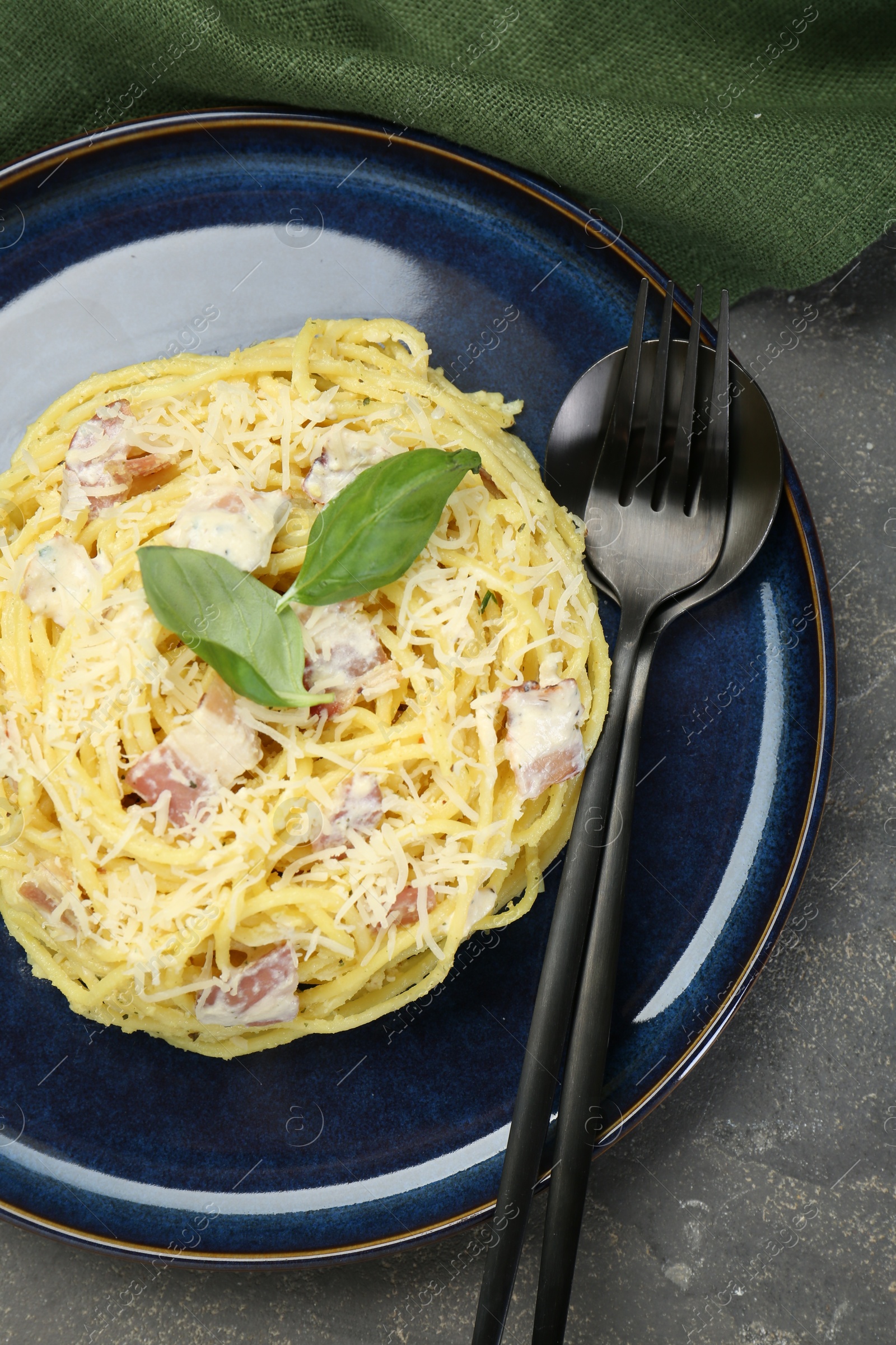 Photo of Plate with delicious pasta Carbonara and cutlery on grey textured table, top view