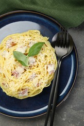 Photo of Plate with delicious pasta Carbonara and cutlery on grey textured table, top view