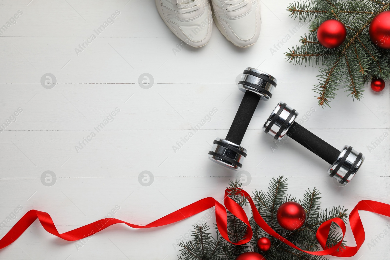 Photo of Dumbbells, sneakers, fir tree branches and Christmas baubles on white table, flat lay. Space for text