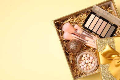 Photo of Makeup brushes, blush and Christmas decor in box on yellow background, above view. Space for text