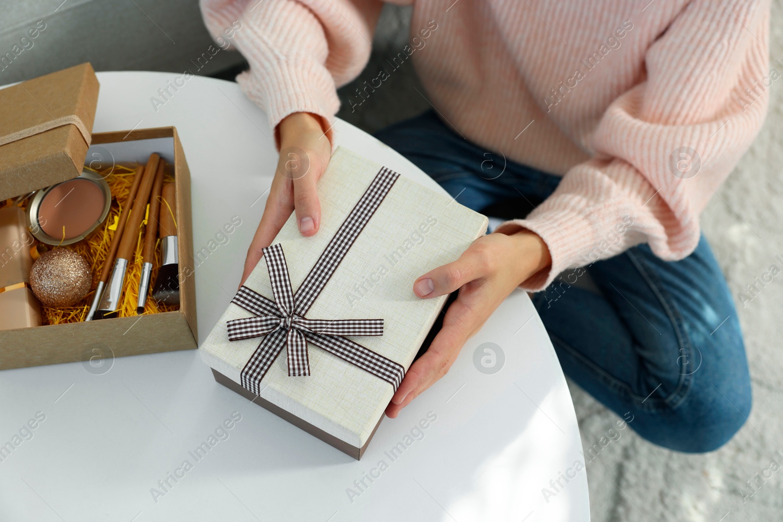 Photo of Woman holding Christmas gift boxes with makeup brushes and cosmetics at white table, above view