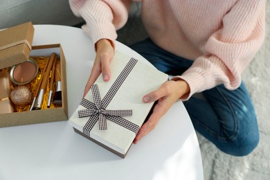 Photo of Woman holding Christmas gift boxes with makeup brushes and cosmetics at white table, above view