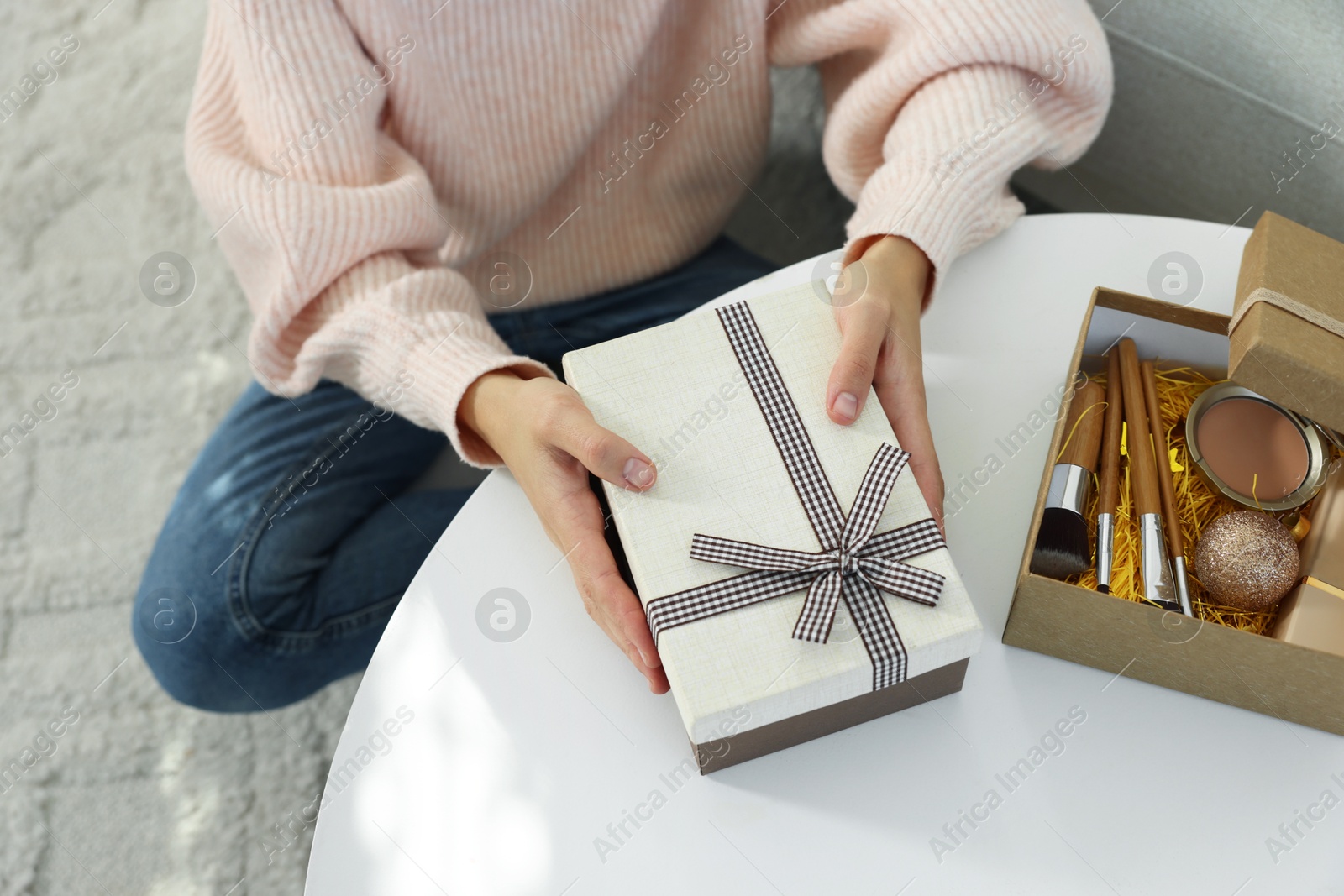 Photo of Woman holding Christmas gift boxes with makeup brushes and cosmetics at white table, above view