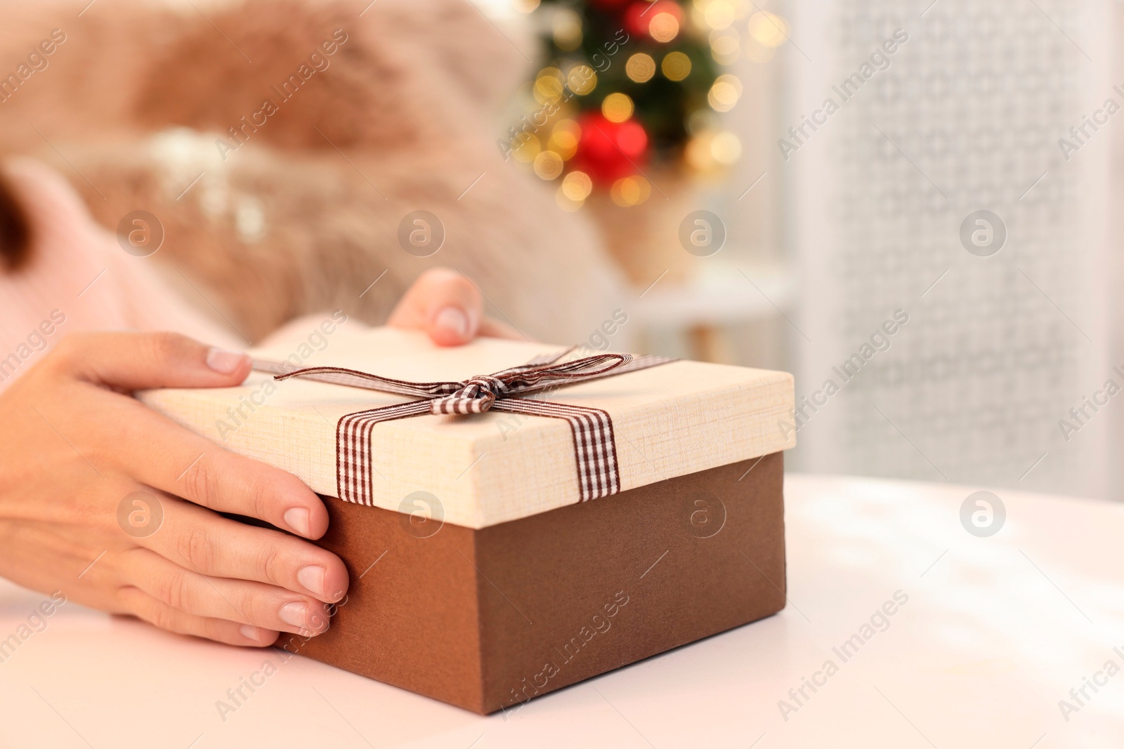 Photo of Woman holding Christmas gift box with makeup brushes and cosmetics at white table, closeup