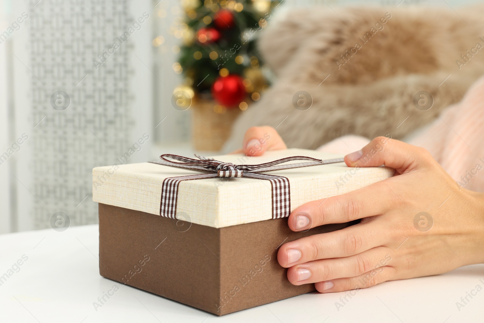 Photo of Woman holding Christmas gift box with makeup brushes and cosmetics at white table, closeup