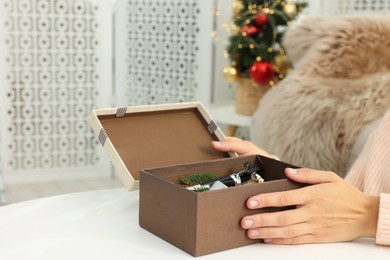 Photo of Woman holding Christmas gift box with makeup brushes and cosmetics at white table, closeup