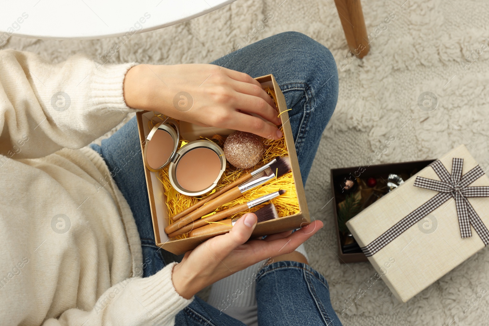 Photo of Woman holding Christmas gift boxes with makeup brushes and cosmetics at home, above view