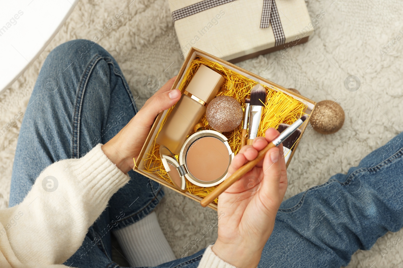 Photo of Woman holding Christmas gift boxes with makeup brushes and cosmetics at home, above view