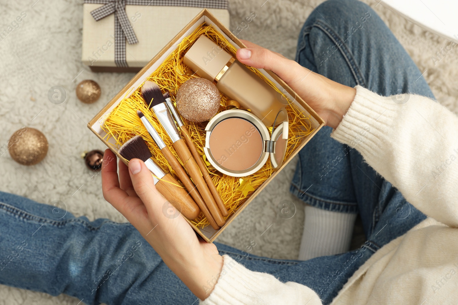 Photo of Woman holding Christmas gift boxes with makeup brushes and cosmetics at home, above view