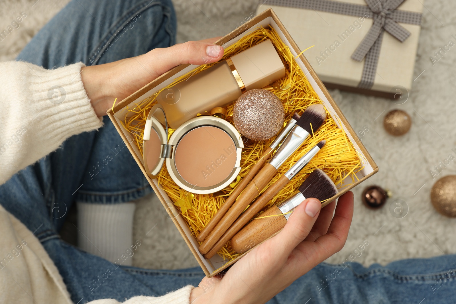 Photo of Woman holding Christmas gift boxes with makeup brushes and cosmetics at home, above view