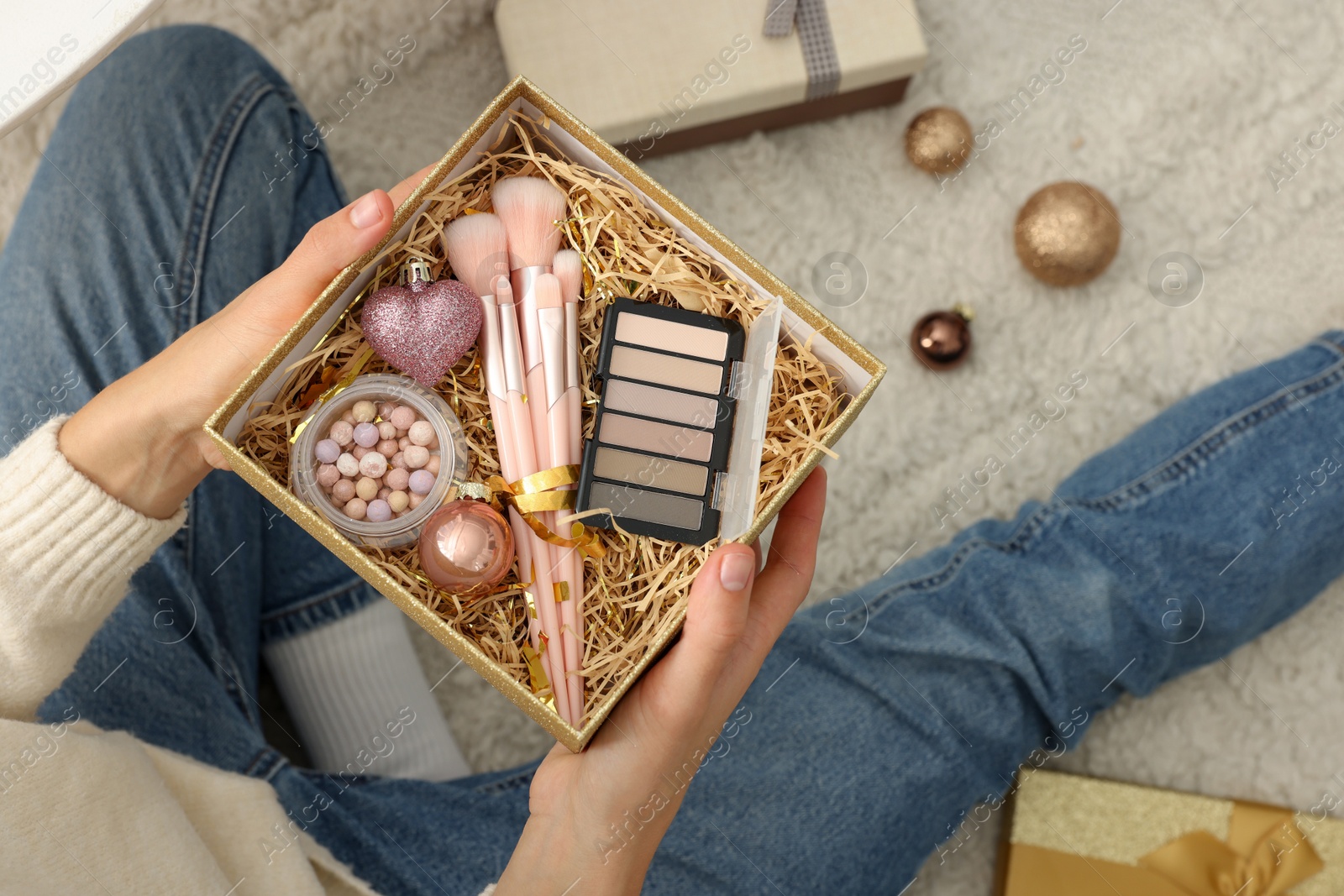 Photo of Woman holding Christmas gift boxes with makeup brushes and cosmetics at home, above view