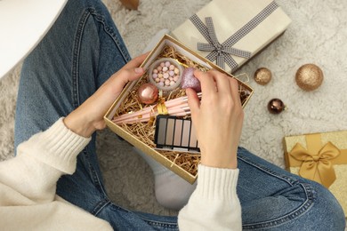 Photo of Woman holding Christmas gift boxes with makeup brushes and cosmetics at home, above view