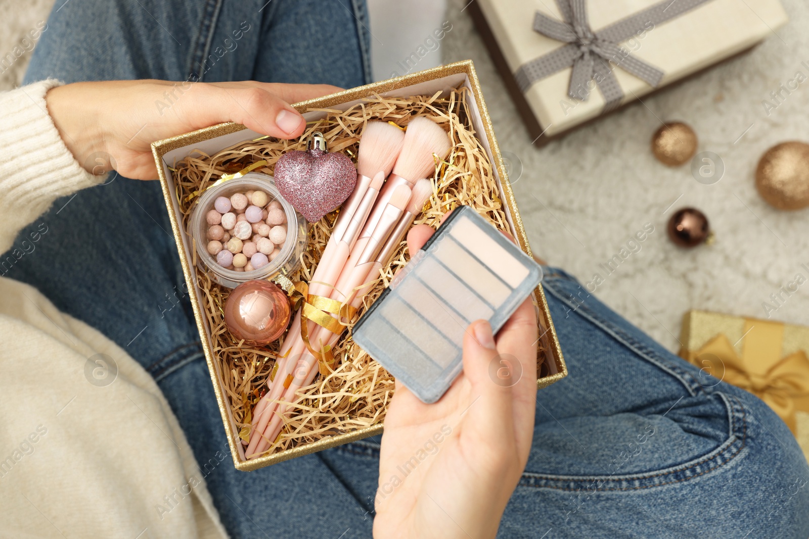 Photo of Woman holding Christmas gift boxes with makeup brushes and cosmetics at home, above view