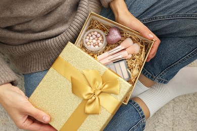 Photo of Woman holding Christmas gift box with makeup brushes and cosmetics at home, above view