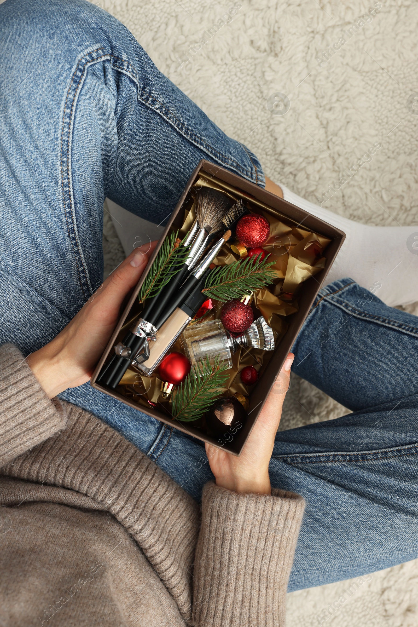 Photo of Woman holding Christmas gift box with makeup brushes and cosmetics at home, above view