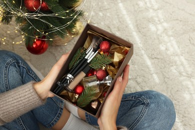 Photo of Woman holding Christmas gift box with makeup brushes and cosmetics at home, above view