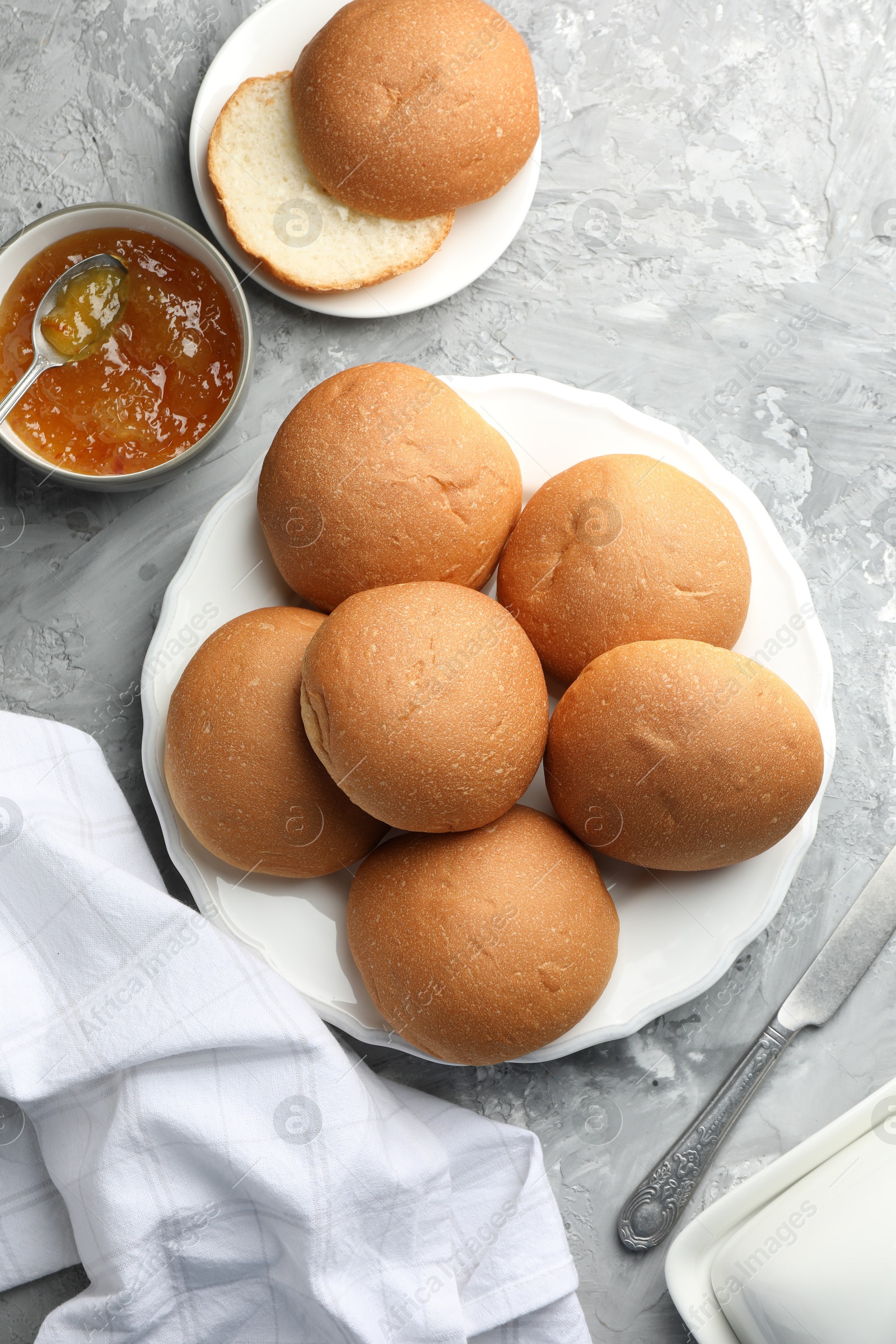 Photo of Fresh tasty buns and jam on grey table, top view