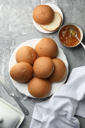 Photo of Fresh tasty buns and jam on grey table, top view