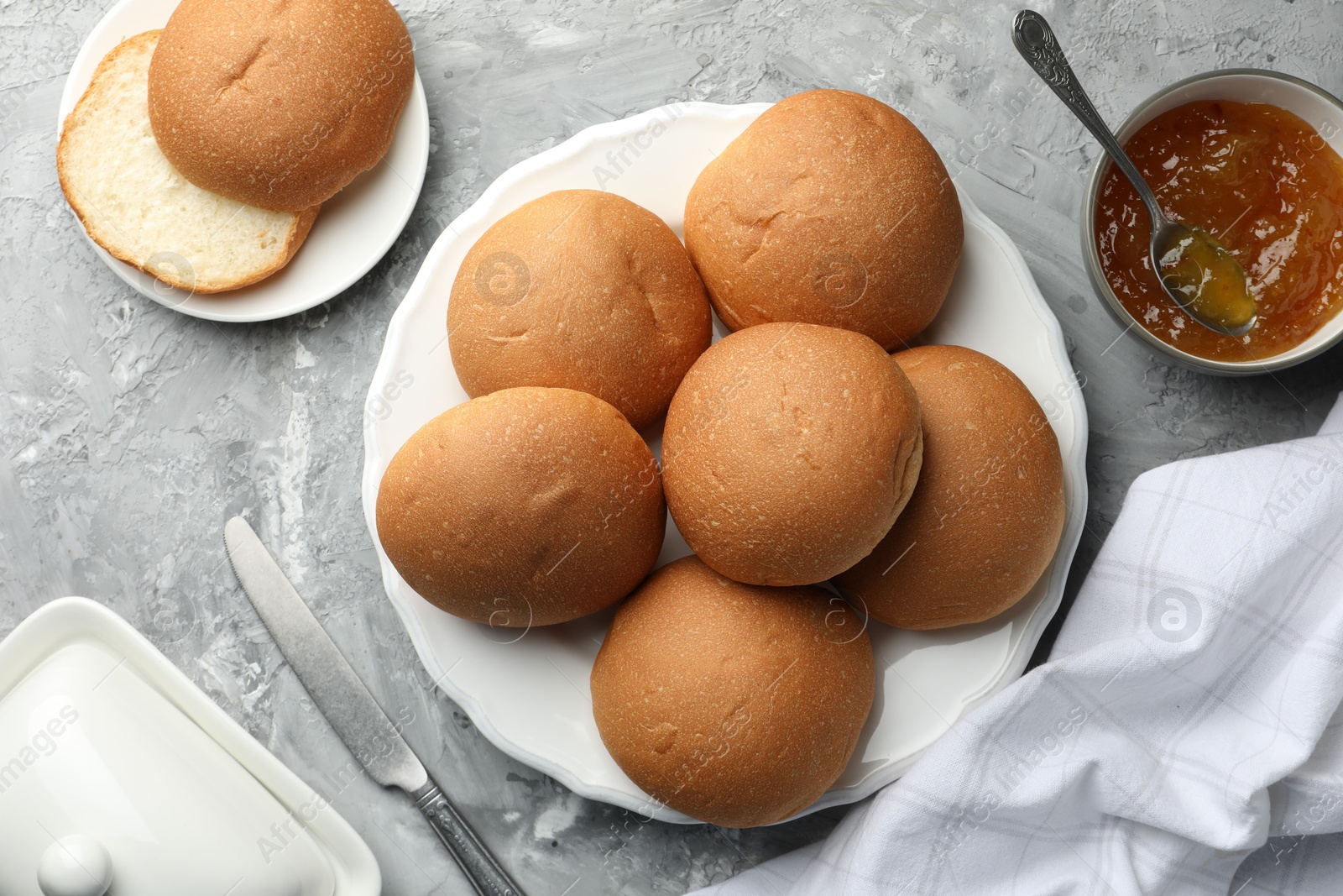 Photo of Fresh tasty buns and jam on grey table, top view