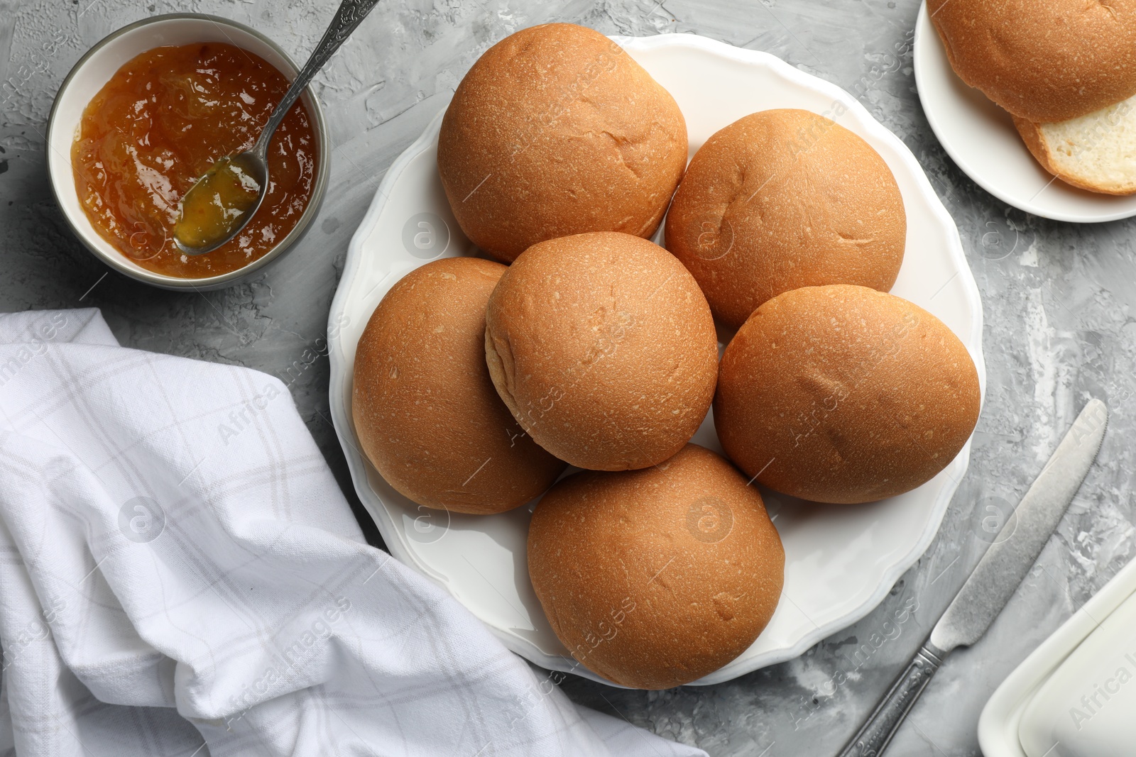 Photo of Fresh tasty buns and jam on grey table, top view