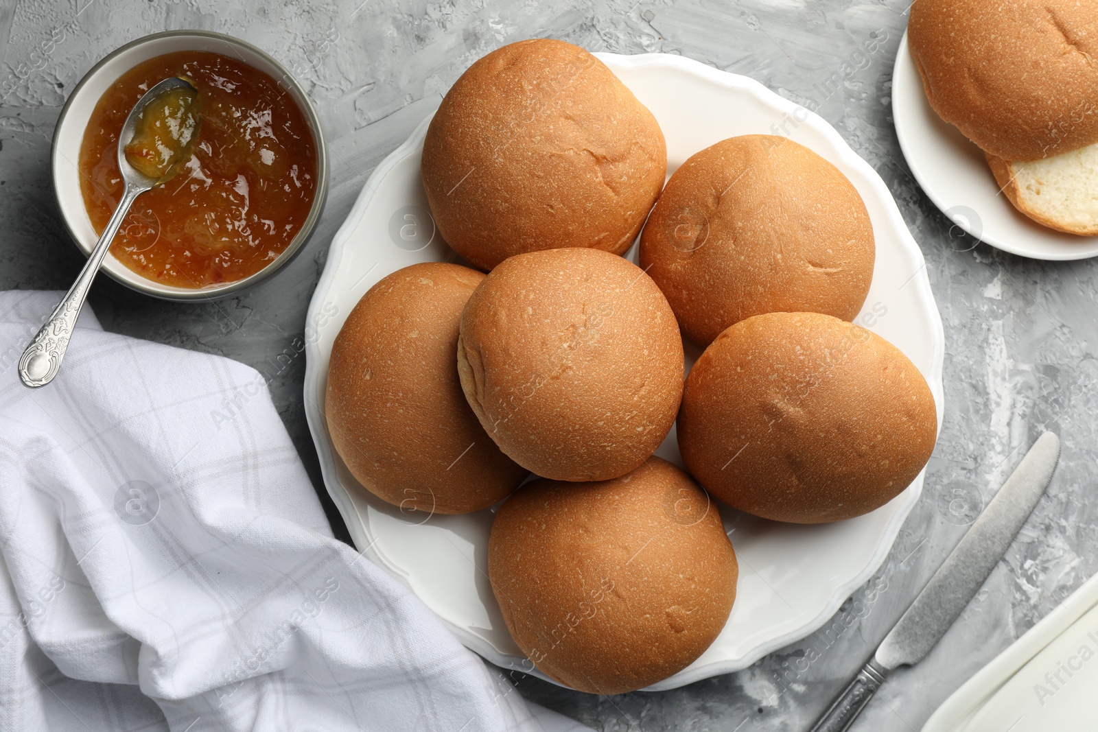 Photo of Fresh tasty buns and jam on grey table, top view