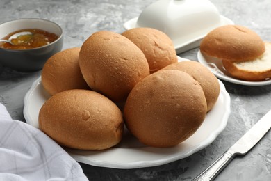 Photo of Fresh tasty buns and jam on grey table, closeup