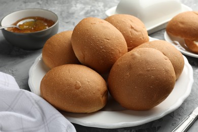 Fresh tasty buns and jam on grey table, closeup