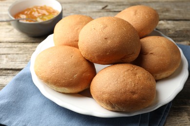 Photo of Fresh tasty buns and jam on wooden table, closeup