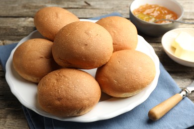 Fresh tasty buns, jam and butter on wooden table, closeup