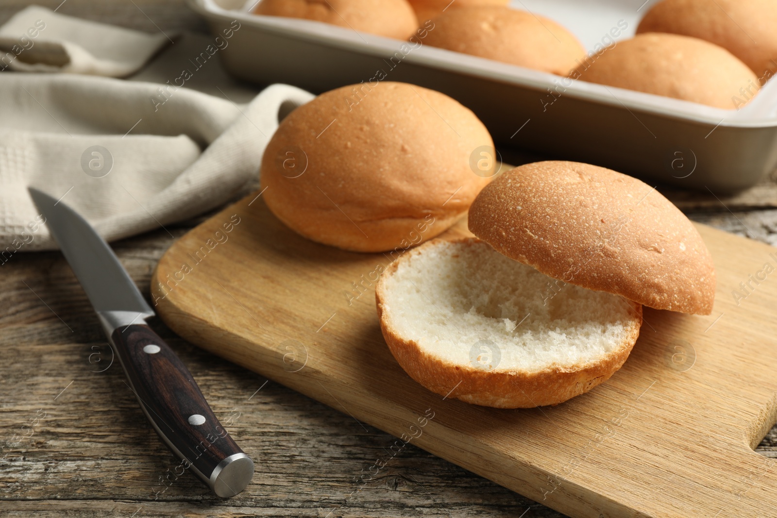 Photo of Fresh tasty buns and knife on wooden table, closeup