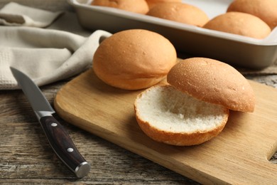 Fresh tasty buns and knife on wooden table, closeup