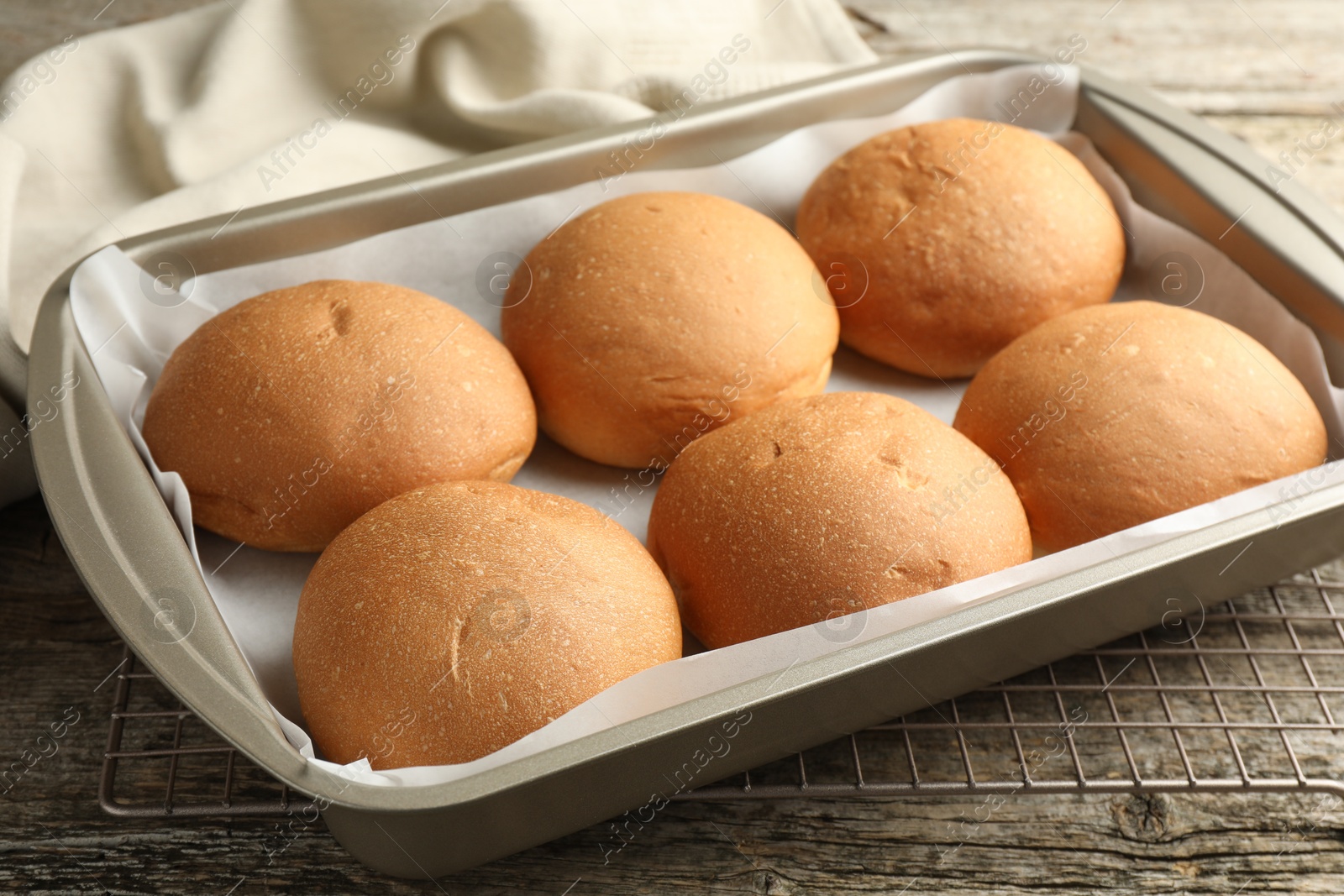 Photo of Fresh tasty buns in baking dish on wooden table, closeup