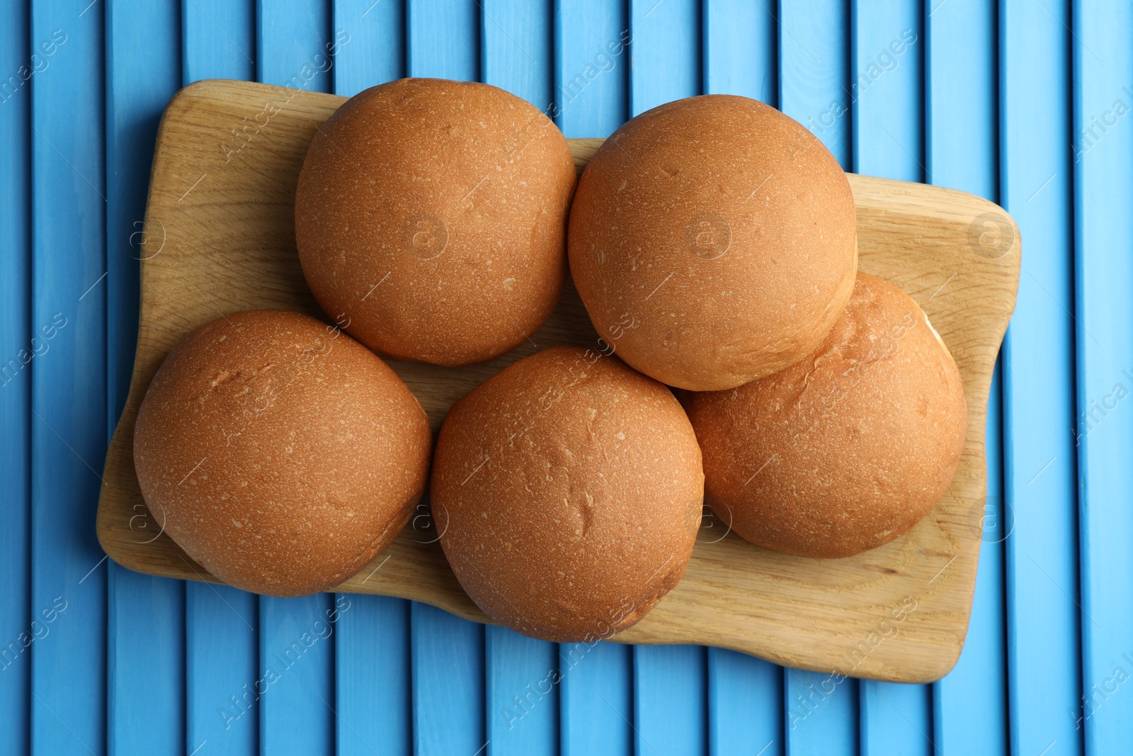 Photo of Fresh tasty buns on light blue wooden surface, top view