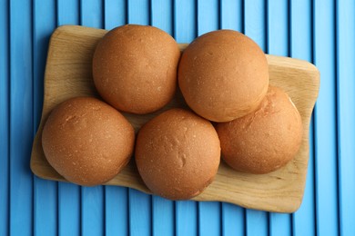 Photo of Fresh tasty buns on light blue wooden surface, top view