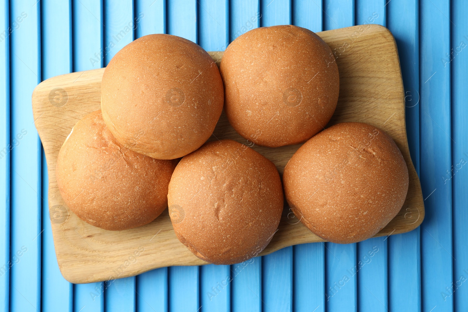 Photo of Fresh tasty buns on light blue wooden surface, top view