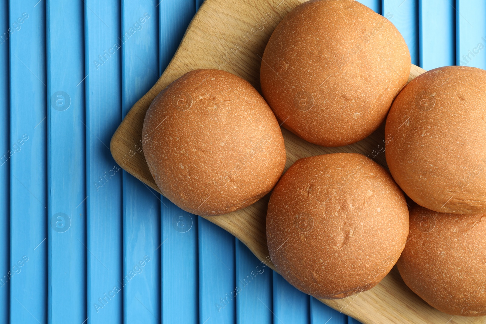 Photo of Fresh tasty buns on light blue wooden surface, top view