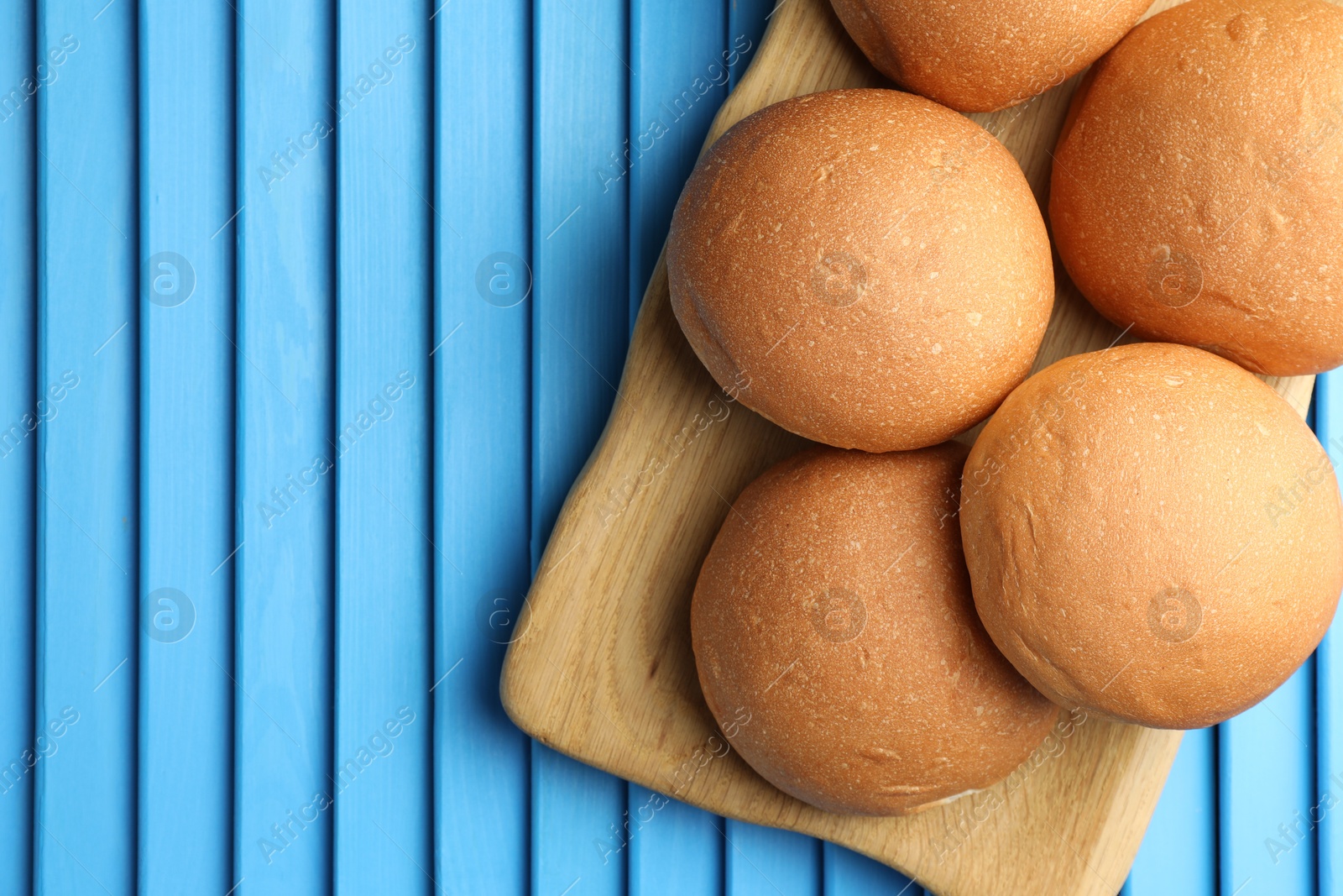 Photo of Fresh tasty buns on light blue wooden surface, top view. Space for text