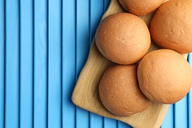 Fresh tasty buns on light blue wooden surface, top view. Space for text