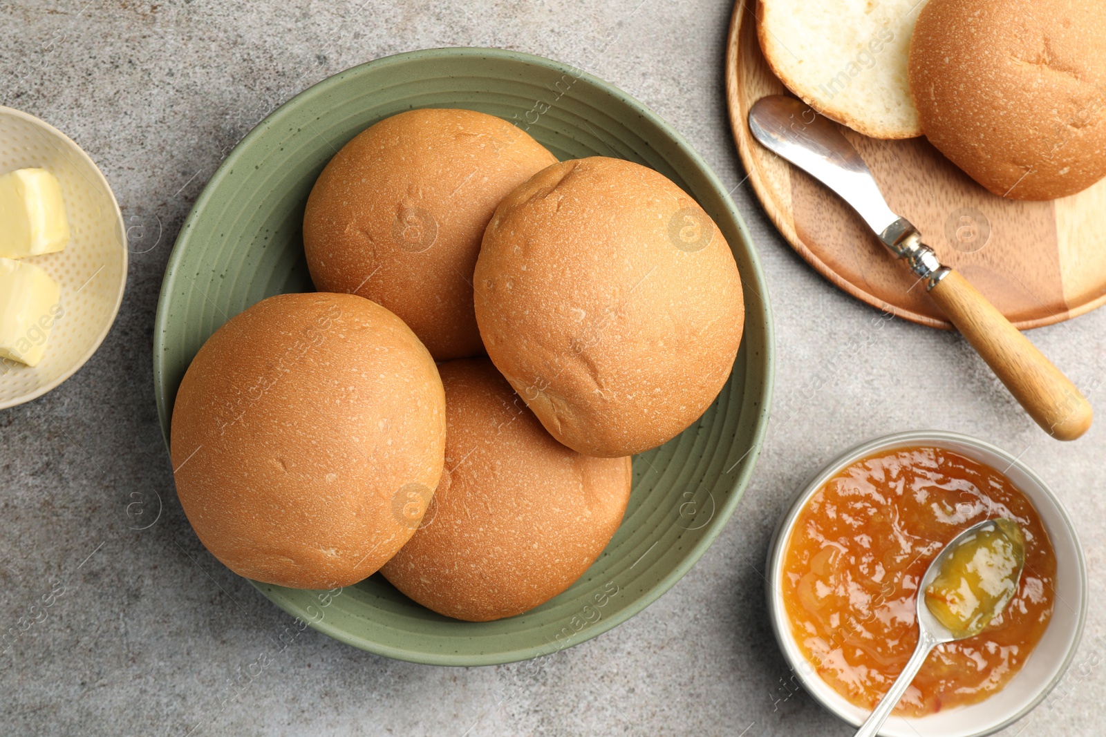 Photo of Fresh tasty buns, jam and butter on grey table, top view